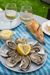 Plate with fresh live oysters with citron, bread, butter and white wine served at restaurant in oyster-farming village, Arcachon bay, Gujan-Mestras port, France