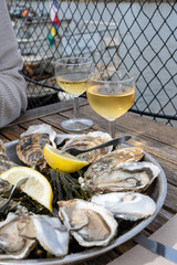 Eating of fresh live oysters with citron at farm cafe in oyster-farming village, with view on boats...
