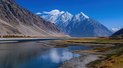 A serene mountain lake with a snow-capped peak in the background, reflecting the blue sky in its calm waters.