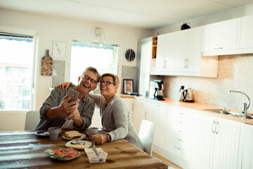 Happy senior mature couple laughing while eating at kitchen table