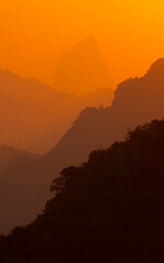 The air, laden with particles and moisture, is crossed by an incredibly orange and reddish light, the silhouettes of the mountains look like fantasy, Laos, Southeast Asia
