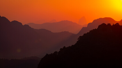 The air, laden with particles and moisture, is crossed by an incredibly orange and reddish light, the silhouettes of the mountains look like fantasy, Laos, Southeast Asia
