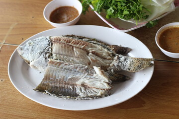 plate of grilled fish with dipping sauce on wood table.