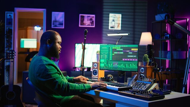 Skilled music producer creating new songs on midi controller synthesizer, working with mixing console and professional software on pc. Artist using piano and mastering acoustical tunes. Camera B.