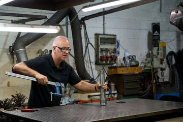 Metalworker using clamp and examining mechanical part in workshop