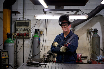 Welder posing with arms crossed in workshop with welding equipment