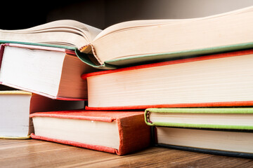 Stacked educational books on a wooden surface with sunlight highlighting their colorful spines