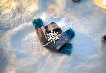 A gray scarf with blue trim lies on a snowy surface, adorned with a silver snowflake pin.