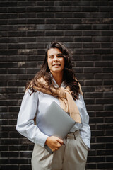 Young businesswoman holding laptop in front of black brick wall