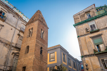 Belltower of pietrasanta complex is rising on the edge of a building in the narrow streets of Napoli old town. Small old brick belltower in the city