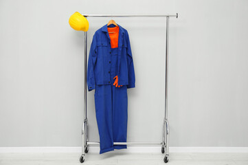 Worker's uniform and hard hat on clothing rack near grey wall indoors