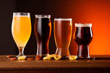 Glasses with different types of beer on wooden table against color background