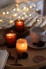 Burning candles, lights, coffee and decor on bed indoors, closeup. Autumn atmosphere
