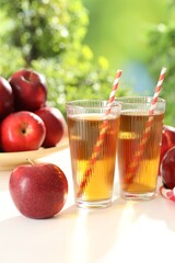 Tasty apple juice in glasses and fresh fruits on white table outdoors