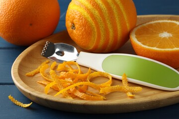 Plate with orange zest, fresh fruit and zester on blue wooden table, closeup