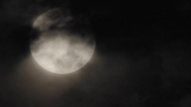 4k video of high thin clouds sailing across the face of a large full moon as it drifts lower in the dark night sky on October 17, 2024.