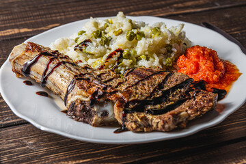 entrecote on the bone with rice, vegetables and tomato sauce on a wooden table