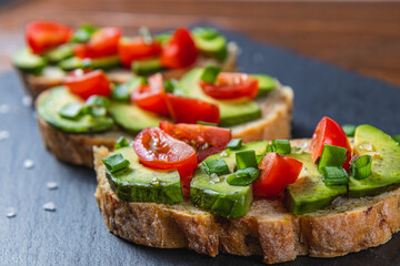 Avocado toast topped with tomato and green onion on a slice of carrot bread