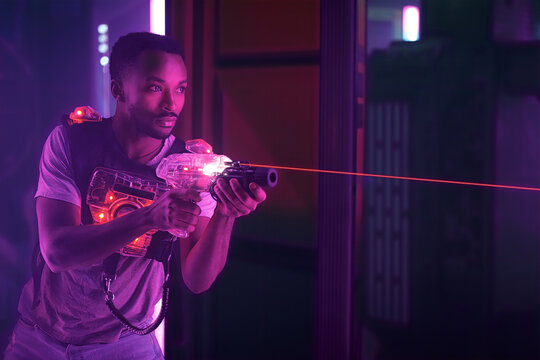 Young man playing laser tag game in neon-lit black light amusement center