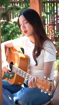 Asian woman singing and playing guitar outdoors in the garden