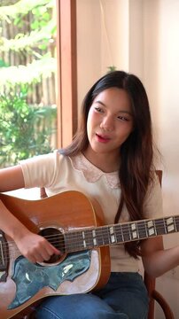Asian woman playing guitar by the window