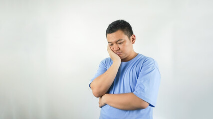 A young Indonesian man wearing a blue t-shirt with a sad face facing downwards