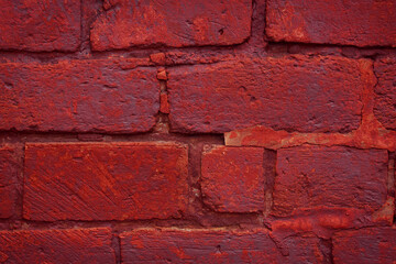 A fragment of a red brick wall with pronounced texture. Natural age defects in the form of cracks and abrasions. Rough surface with traces of dried paint.