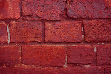 A fragment of a red brick wall with pronounced texture. Natural age defects in the form of cracks and abrasions. Rough surface with traces of dried paint.