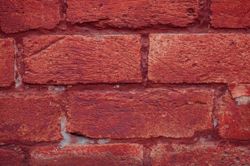 A fragment of a red brick wall with pronounced texture. Natural age defects in the form of cracks and abrasions. Rough surface with traces of dried paint.