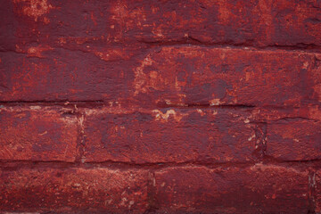 A fragment of a red brick wall with pronounced texture. Natural age defects in the form of cracks and abrasions. Rough surface with traces of dried paint.