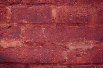 A fragment of a red brick wall with pronounced texture. Natural age defects in the form of cracks and abrasions. Rough surface with traces of dried paint.