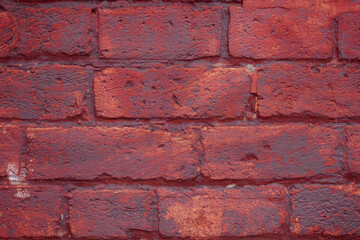 A fragment of a red brick wall with pronounced texture. Natural age defects in the form of cracks and abrasions. Rough surface with traces of dried paint.