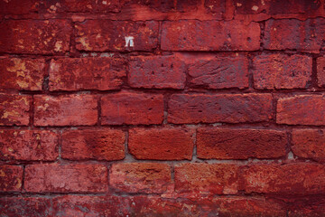 A fragment of a red brick wall with pronounced texture. Natural age defects in the form of cracks and abrasions. Rough surface with traces of dried paint.