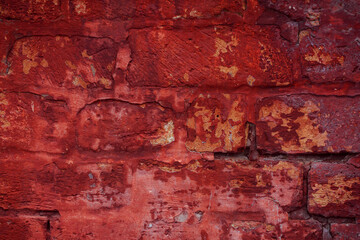 A fragment of a red brick wall with pronounced texture. Natural age defects in the form of cracks and abrasions. Rough surface with traces of dried paint.