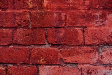 A fragment of a red brick wall with pronounced texture. Natural age defects in the form of cracks and abrasions. Rough surface with traces of dried paint.