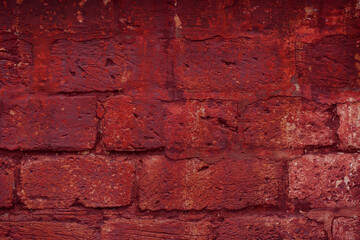 A fragment of a red brick wall with pronounced texture. Natural age defects in the form of cracks and abrasions. Rough surface with traces of dried paint.