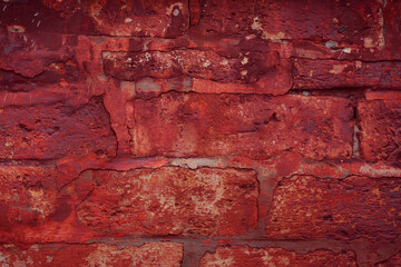 A fragment of a red brick wall with pronounced texture. Natural age defects in the form of cracks and abrasions. Rough surface with traces of dried paint.