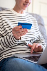 Unrecognizable smiling woman hands with credit card working on laptop. Online purchasing behavior,...