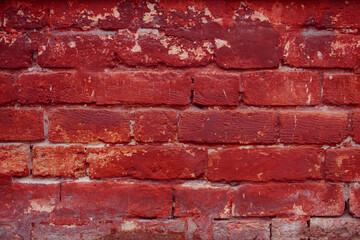 A fragment of a red brick wall with pronounced texture. Natural age defects in the form of cracks and abrasions. Rough surface with traces of dried paint.