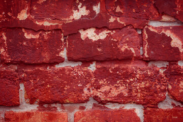 A fragment of a red brick wall with pronounced texture. Natural age defects in the form of cracks and abrasions. Rough surface with traces of dried paint.