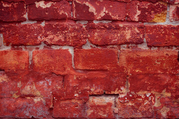 A fragment of a red brick wall with pronounced texture. Natural age defects in the form of cracks and abrasions. Rough surface with traces of dried paint.