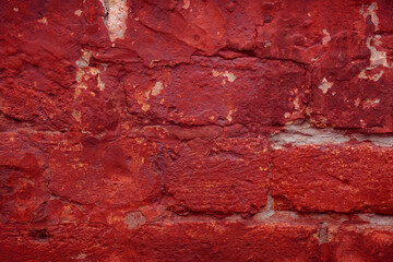 A fragment of a red brick wall with pronounced texture. Natural age defects in the form of cracks and abrasions. Rough surface with traces of dried paint.