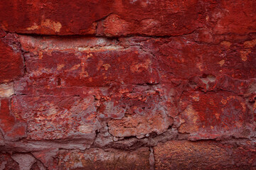 Obraz premium A fragment of a red brick wall with pronounced texture. Natural age defects in the form of cracks and abrasions. Rough surface with traces of dried paint.
