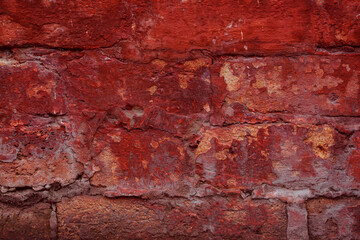 A fragment of a red brick wall with pronounced texture. Natural age defects in the form of cracks and abrasions. Rough surface with traces of dried paint.