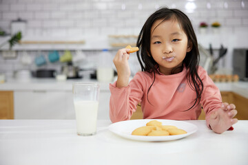 Portrait child girl enjoy eating cookies and drinking milk in the kitchen