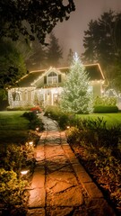 Fototapeta premium Traditional home and yard illuminated by warm Christmas string lights, featuring a festive outdoor tree and a glowing stone pathway on a foggy winter night.