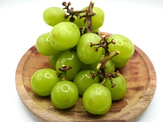 Cluster of fresh muscat grapes or green grapes or anggur sultan isolated on a wooden plate against a white background