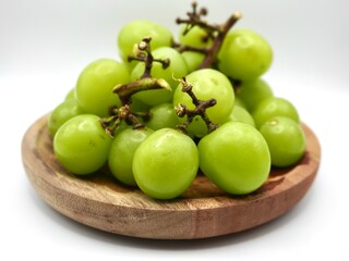 Close up image of fresh muscat grapes or green grapes or anggur sultan isolated on a wooden plate against a white background. Healthy food for a diet.