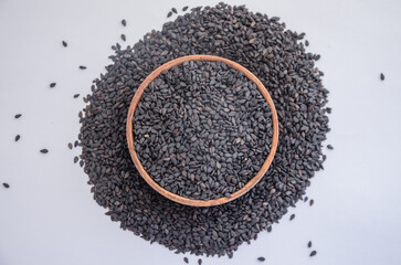 Black sesame seeds in a wooden plate on a light background