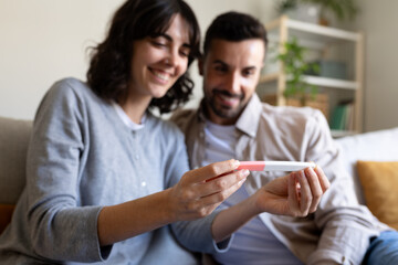 Happy caucasian couple looking at positive pregnancy test together at home. Selective focus on...